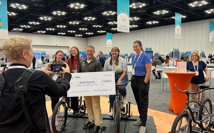 Nine13sports’ Nathan Smurdon, flanked by bikers who took part in the challenge, receives a $15,000 check from Tyler.